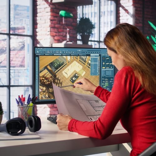 Freelancer designer decorates apartment floor plan using blueprints on pc, using architectural software to configure elements. Woman uses interface to enable rendering and 3D modeling. Camera B.